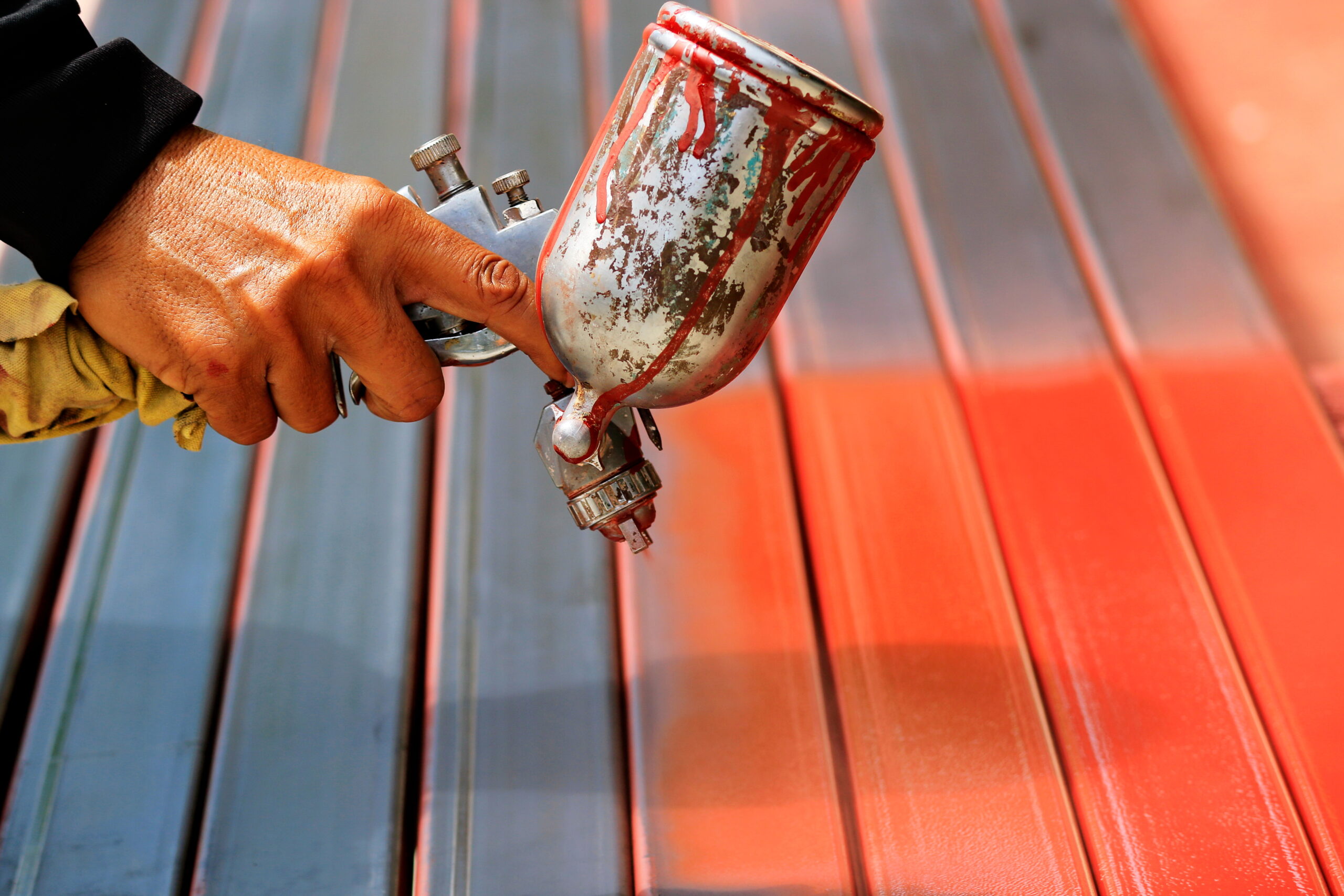 Worker holding a spray gun painting the exterior of a deck a bright red color