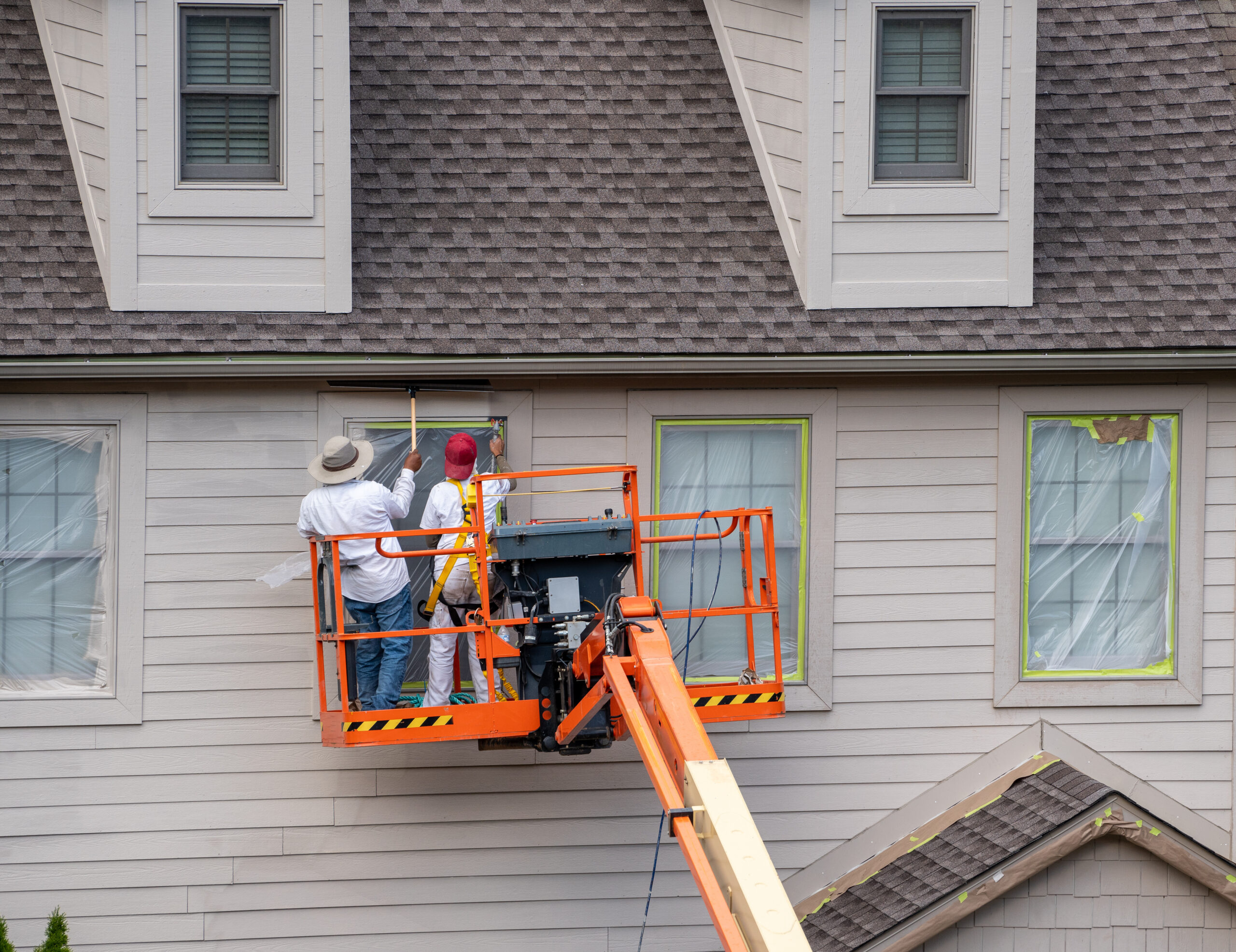 Professionals in scissor lift as they paint the exterior of a home