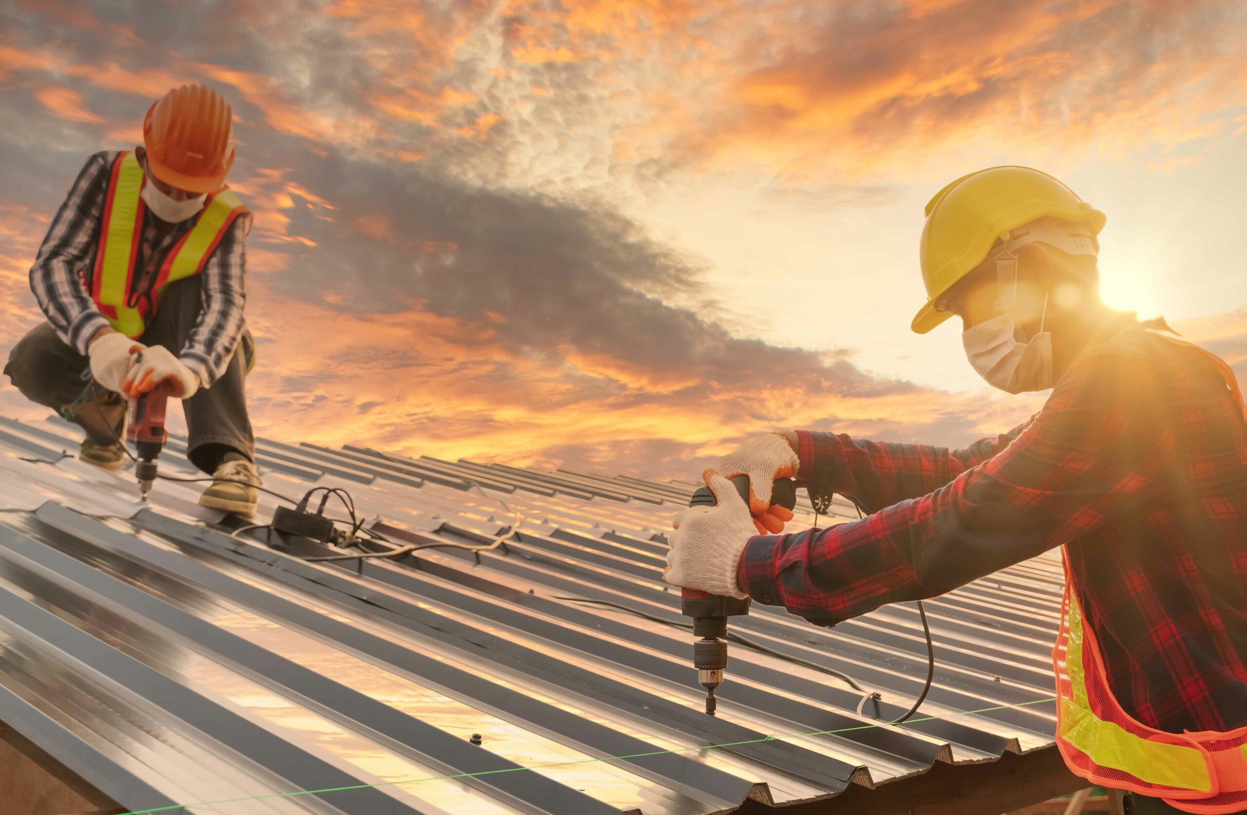 Metal roof being installed on building by two workers