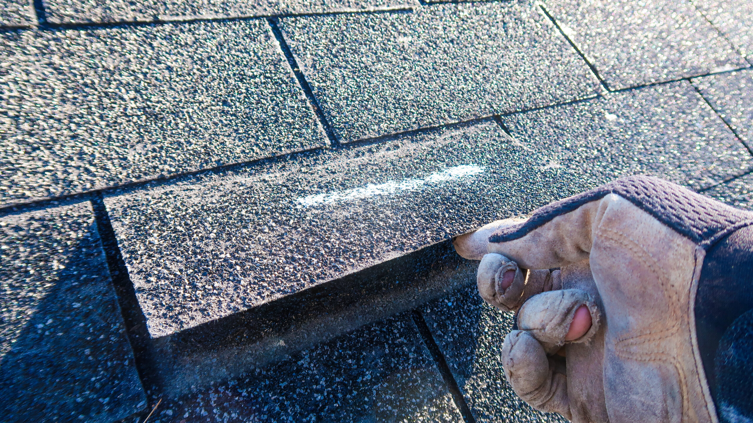 Technician lifting damaged shingle showing roof repair is needed