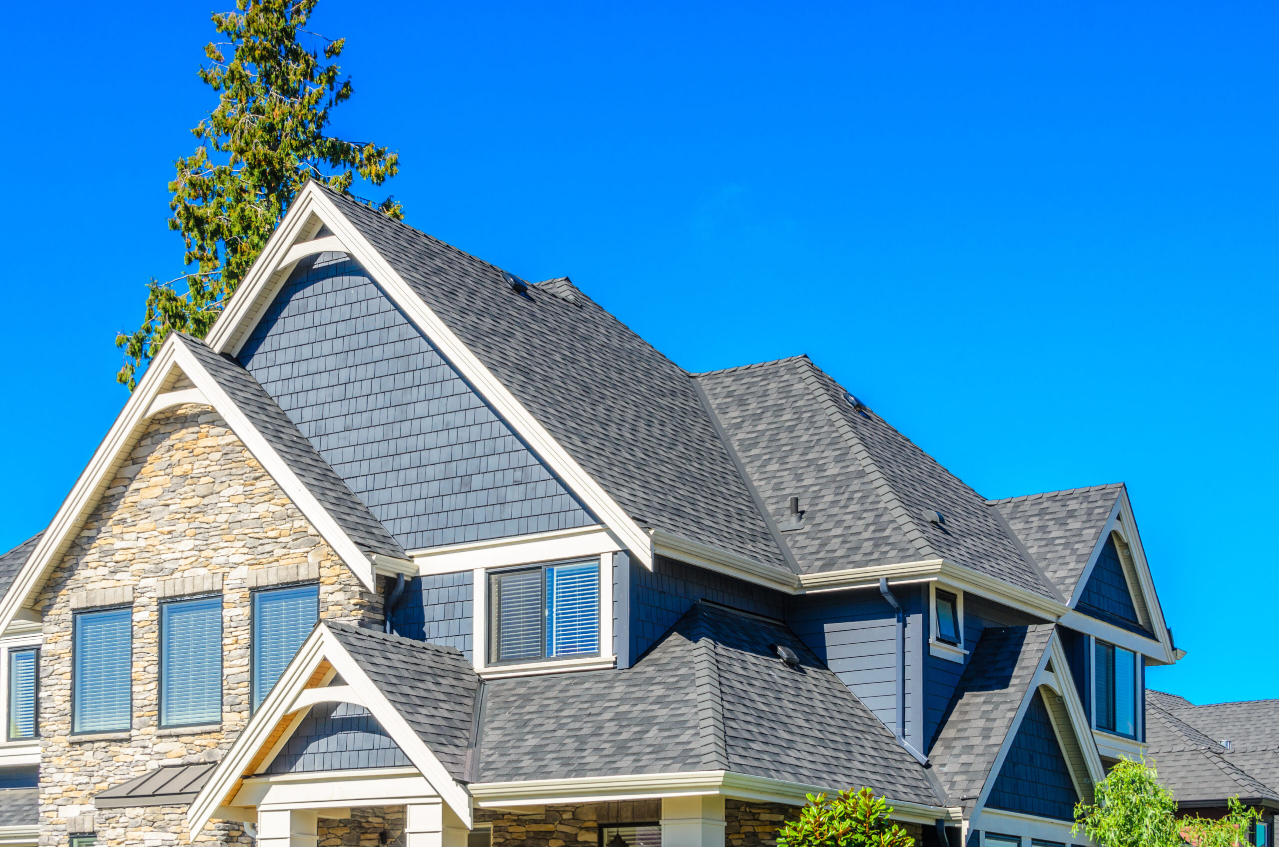 Peaked gray asphalt roof on house with brick and siding