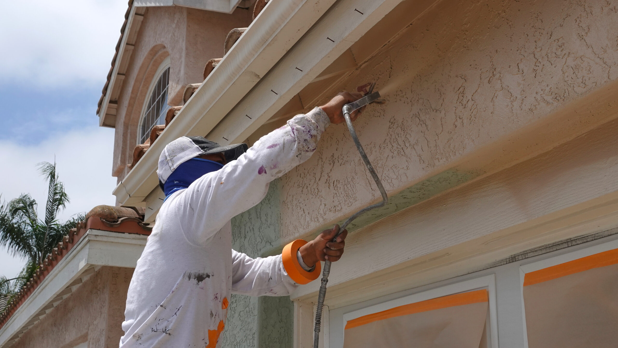 Contractor using spray gun to paint a stucco home