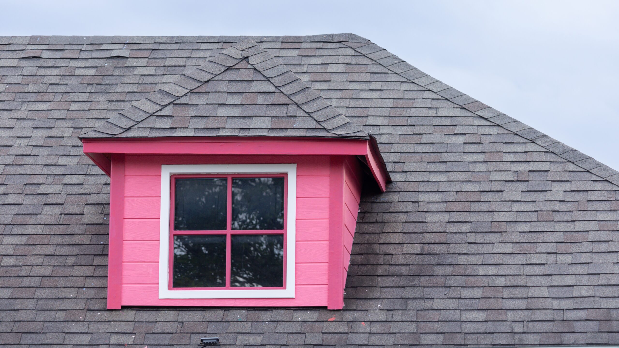 Home roof gable with pink siding and shingle roofing