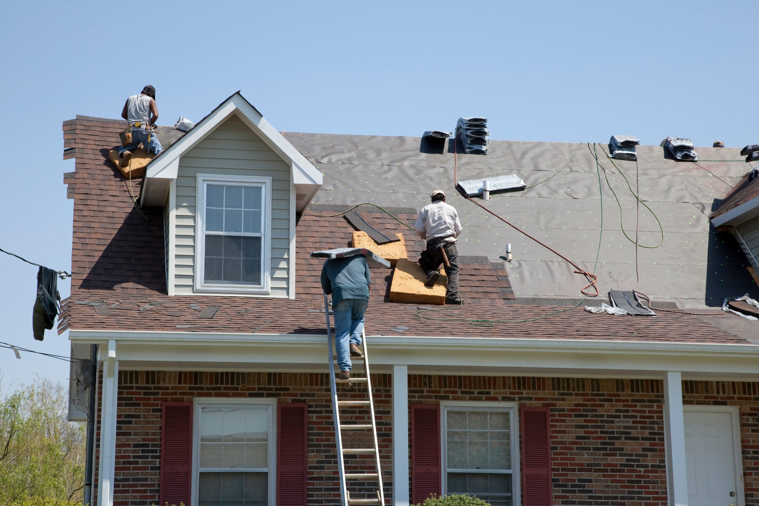 Roofers installing new asphalt shingles on roof of brick home